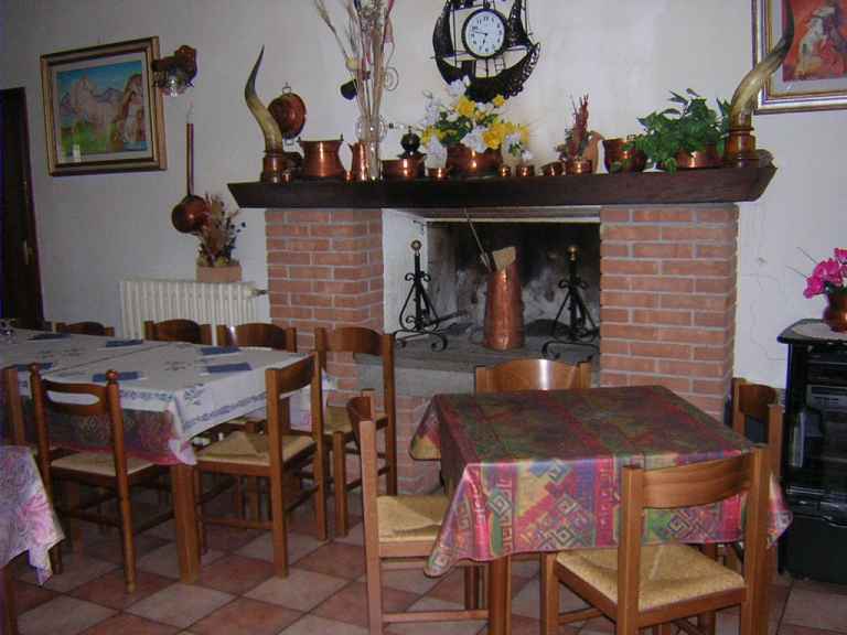 Indoor dining area with a brick fireplace decorated with copper pots and dried flowers, wooden tables with patterned tablecloths