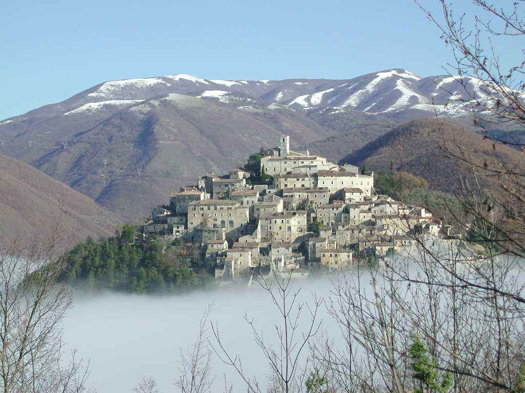 Hilltop stone village surrounded by mist and mountains with snow-capped peaks, blue sky