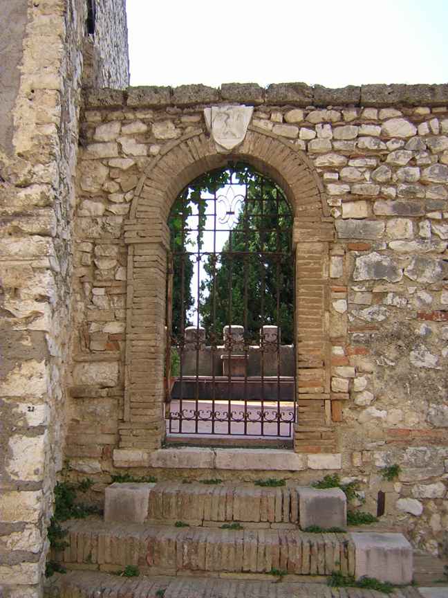 Stone archway with wrought-iron gate leading to a garden area, decorative stonework above the arch