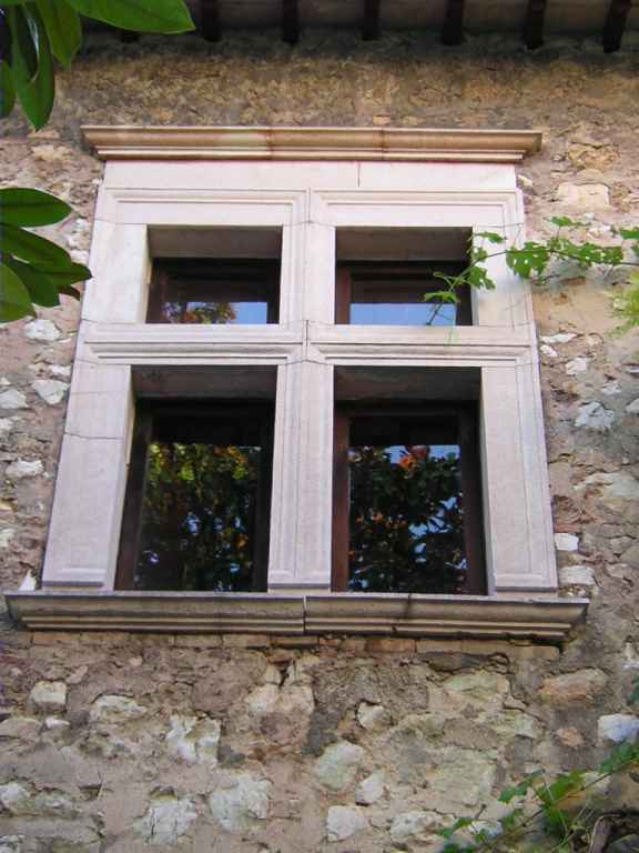 Stone wall with a decorative divided window framed in light-colored stone, greenery at edges